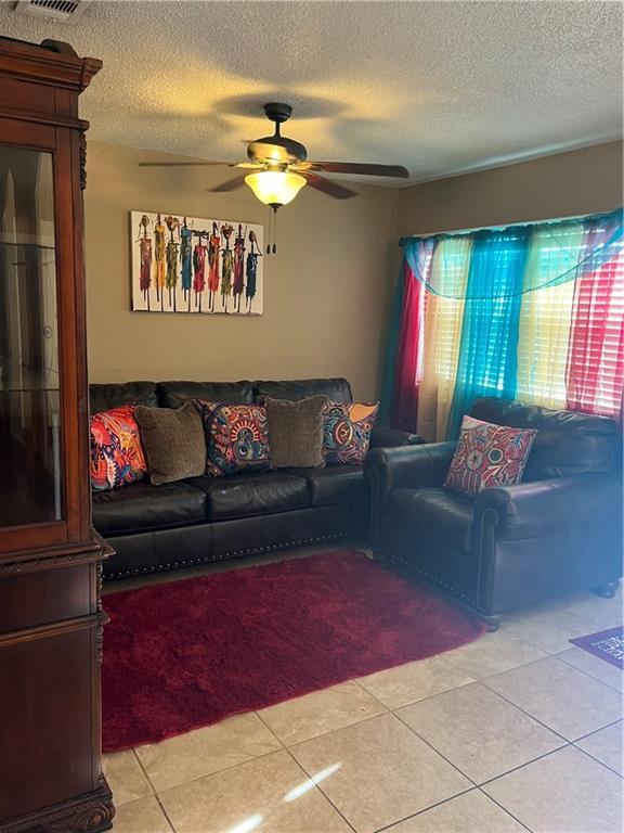 tiled living room with ceiling fan and a textured ceiling