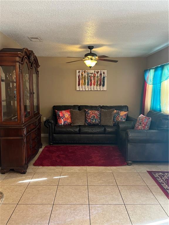 living room featuring ceiling fan, light tile patterned floors, and a textured ceiling