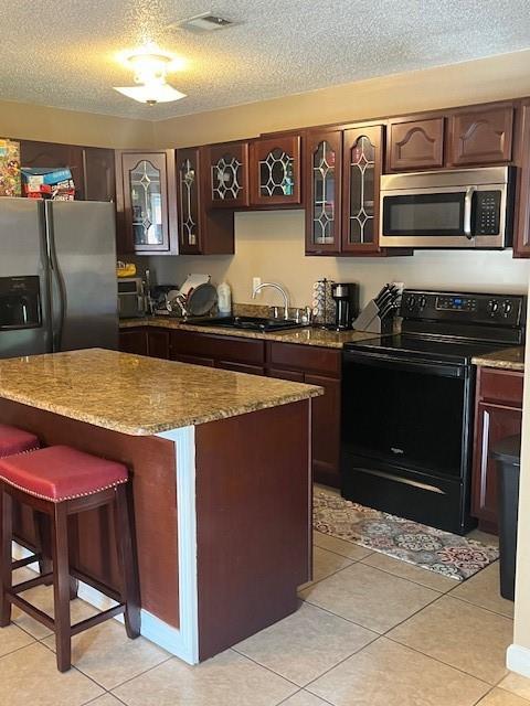 kitchen with appliances with stainless steel finishes, a center island, a textured ceiling, and light tile patterned flooring