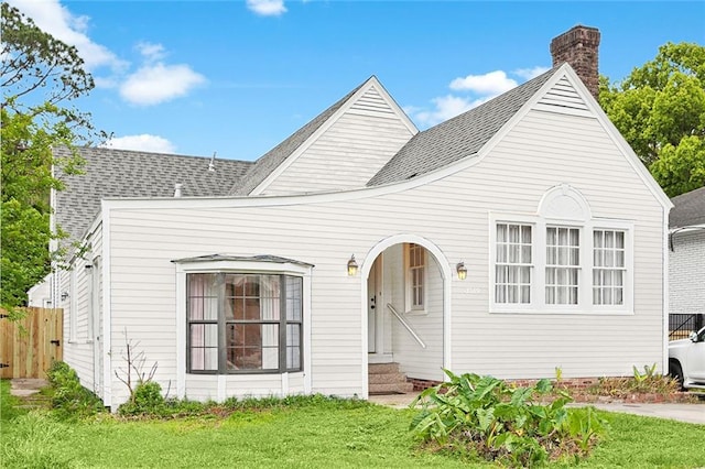 view of front of property featuring entry steps, fence, roof with shingles, a front yard, and a chimney