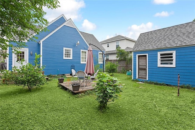 rear view of property with a deck, a lawn, fence, and roof with shingles