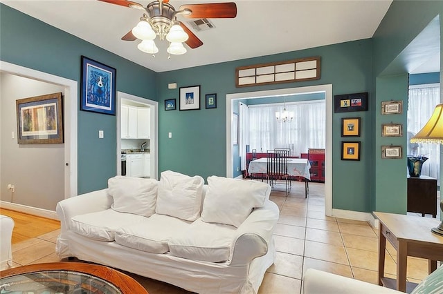 living area with light tile patterned flooring, visible vents, plenty of natural light, and ceiling fan with notable chandelier