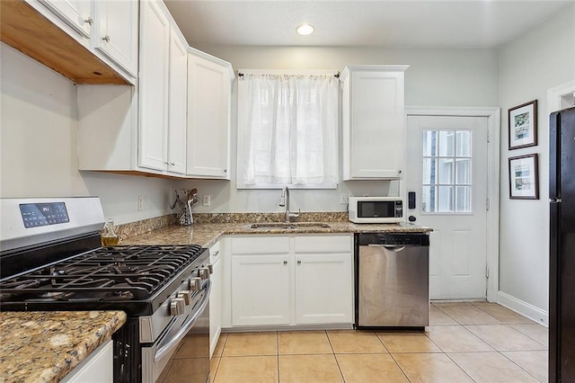 kitchen with light tile patterned floors, light stone countertops, a sink, stainless steel appliances, and white cabinets