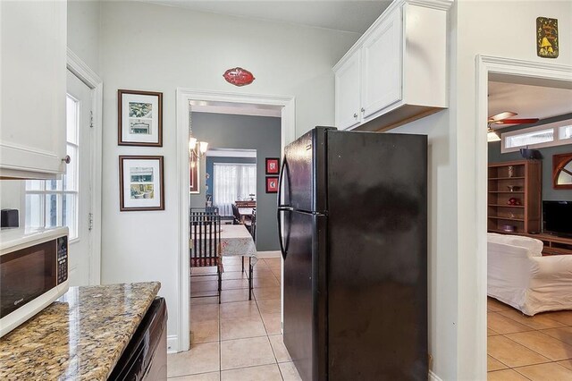 kitchen featuring light tile patterned floors, light stone countertops, white cabinetry, and black fridge