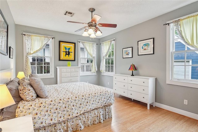 bedroom with multiple windows, wood finished floors, visible vents, and baseboards