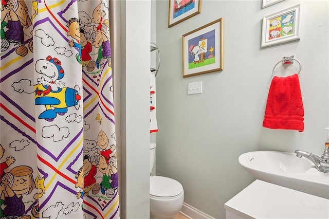 bathroom featuring a sink, curtained shower, baseboards, and toilet