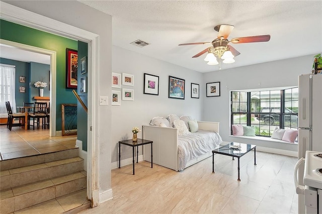 living area with a textured ceiling, a ceiling fan, visible vents, and baseboards