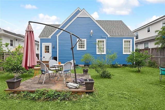 rear view of house with a lawn, roof with shingles, a deck, and fence