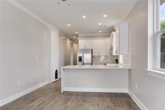 kitchen featuring kitchen peninsula, appliances with stainless steel finishes, light wood-type flooring, crown molding, and white cabinetry