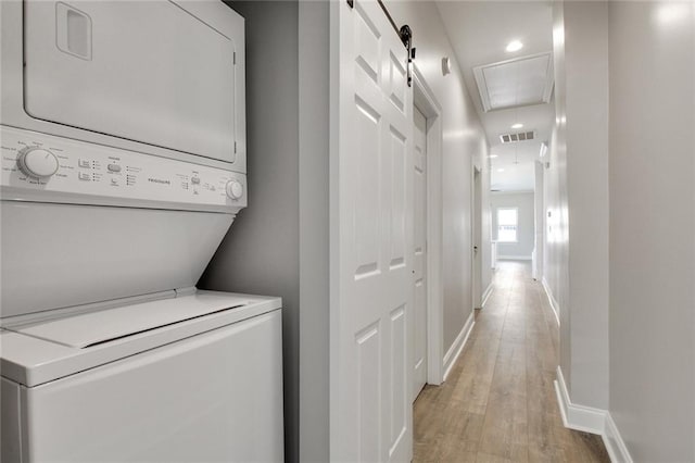 laundry area with stacked washer / drying machine, a barn door, and light wood-type flooring