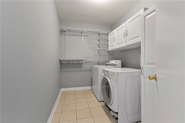 laundry area featuring washing machine and clothes dryer, light tile patterned floors, and cabinets