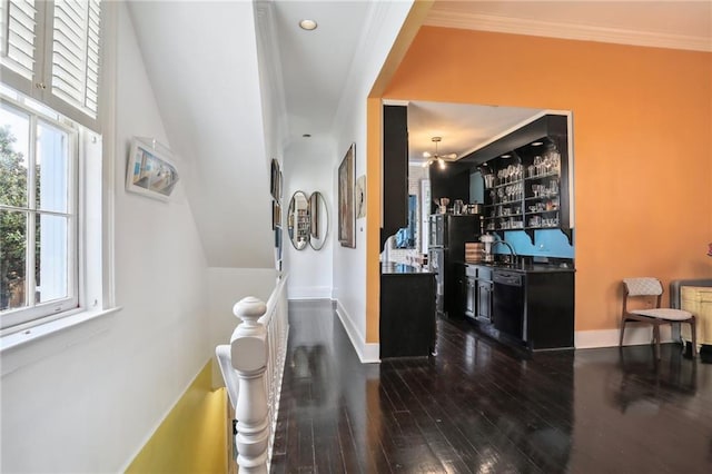 hall featuring baseboards, a sink, ornamental molding, and dark wood-style flooring