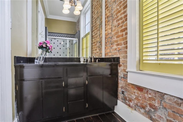 bathroom featuring a notable chandelier, crown molding, vanity, and brick wall