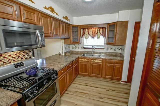 kitchen with decorative backsplash, light wood-type flooring, sink, stainless steel appliances, and a textured ceiling