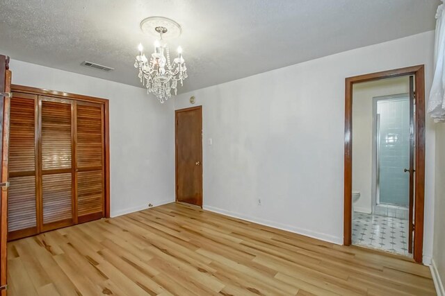 unfurnished bedroom with a closet, connected bathroom, light hardwood / wood-style floors, a notable chandelier, and a textured ceiling