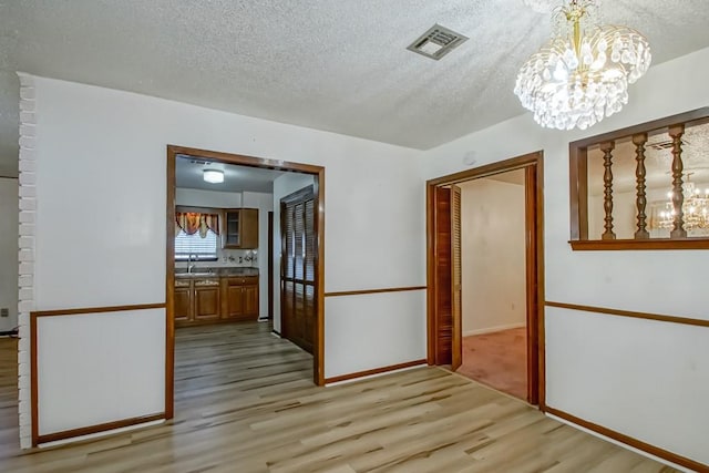 corridor featuring a textured ceiling, sink, a chandelier, and light hardwood / wood-style flooring