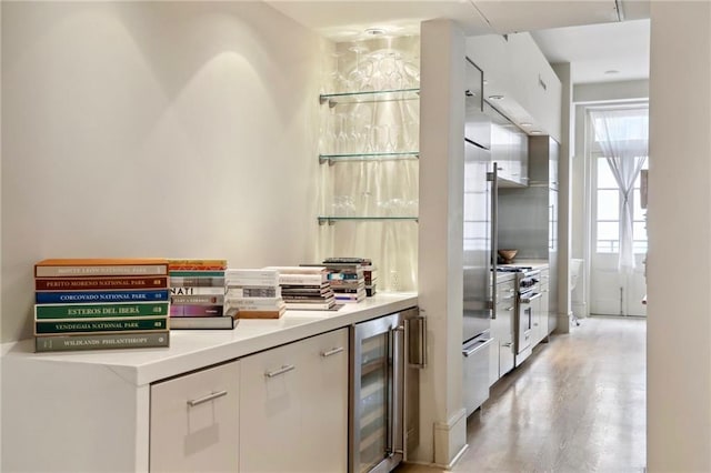 kitchen with light wood-type flooring, high end stainless steel range, white cabinetry, and beverage cooler