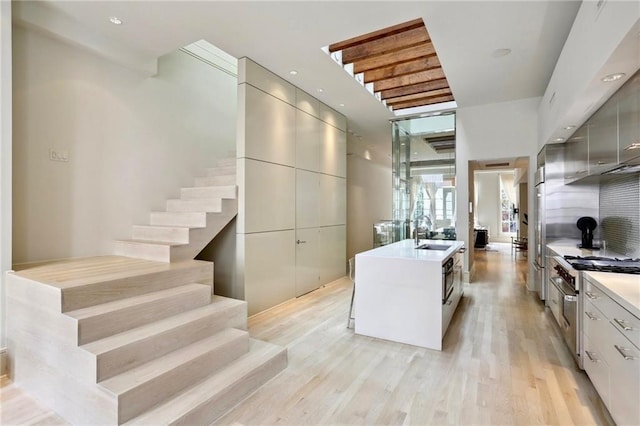 kitchen featuring light hardwood / wood-style flooring, sink, gray cabinets, stainless steel stove, and a kitchen island with sink