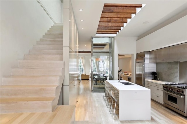 kitchen with an island with sink, sink, tasteful backsplash, high end appliances, and a kitchen bar