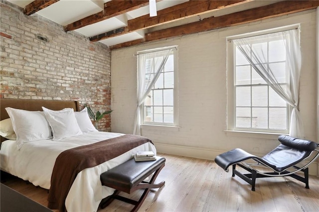 bedroom featuring light hardwood / wood-style floors, beamed ceiling, and brick wall