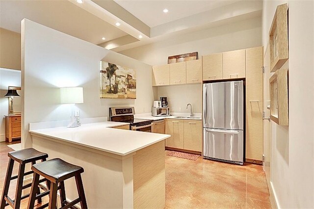 kitchen with appliances with stainless steel finishes, sink, cream cabinetry, a kitchen breakfast bar, and kitchen peninsula