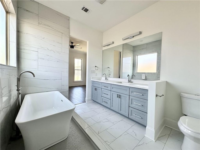 bathroom with ceiling fan, vanity, toilet, and a washtub