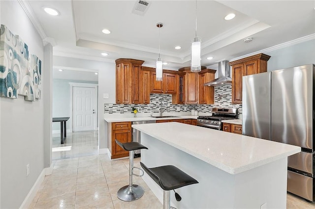 kitchen with stainless steel appliances, a tray ceiling, decorative light fixtures, and wall chimney exhaust hood