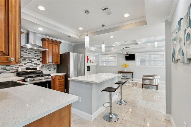 kitchen featuring light stone countertops, decorative backsplash, gas stove, crown molding, and wall chimney range hood