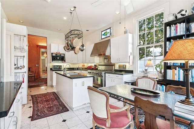 kitchen with a wealth of natural light, a kitchen island with sink, stainless steel appliances, and wall chimney range hood