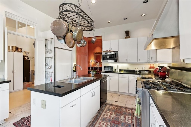 kitchen featuring appliances with stainless steel finishes, wall chimney range hood, sink, a center island with sink, and white cabinetry