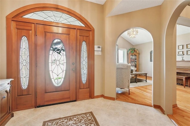 entryway featuring light tile patterned floors, vaulted ceiling, and a notable chandelier