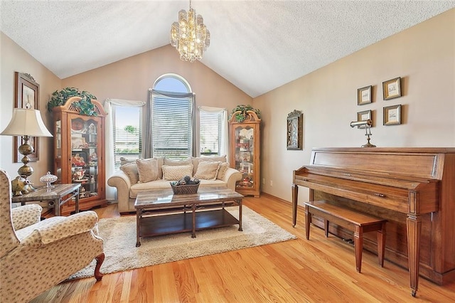 living room with a textured ceiling, a notable chandelier, lofted ceiling, and light wood-type flooring