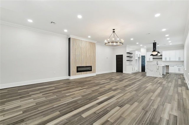 unfurnished living room featuring ornamental molding, sink, a fireplace, hardwood / wood-style floors, and a chandelier