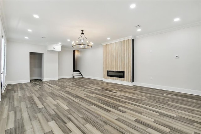 unfurnished living room with a large fireplace, ornamental molding, light wood-type flooring, and a notable chandelier