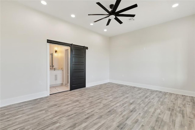 unfurnished bedroom featuring ceiling fan, a barn door, light wood-type flooring, and connected bathroom