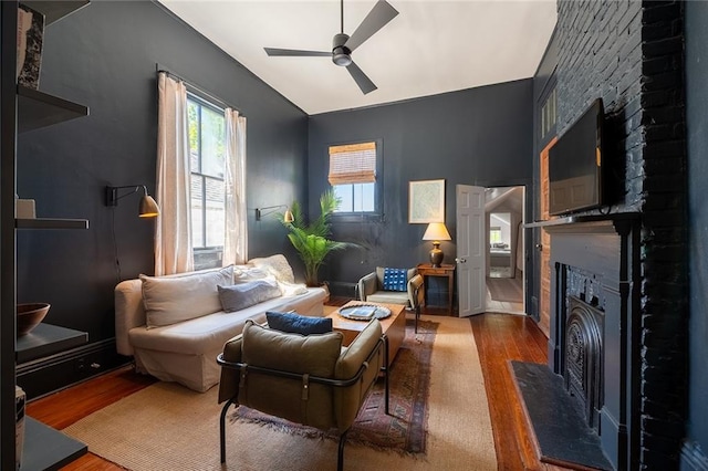 living room with wood-type flooring, a large fireplace, ceiling fan, and lofted ceiling