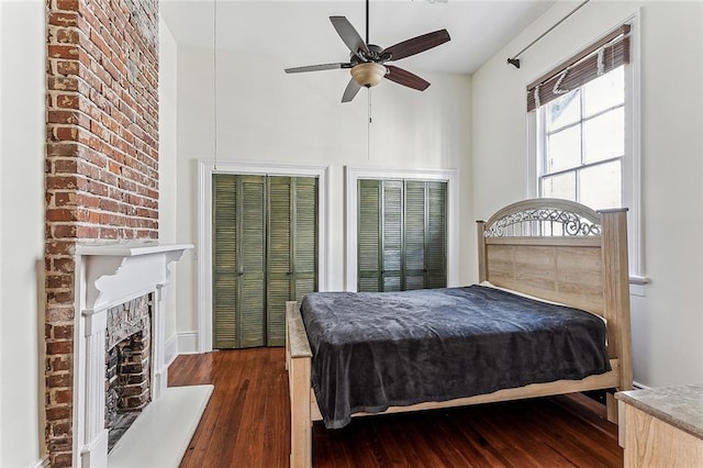 bedroom with ceiling fan, multiple closets, a fireplace, and dark hardwood / wood-style flooring