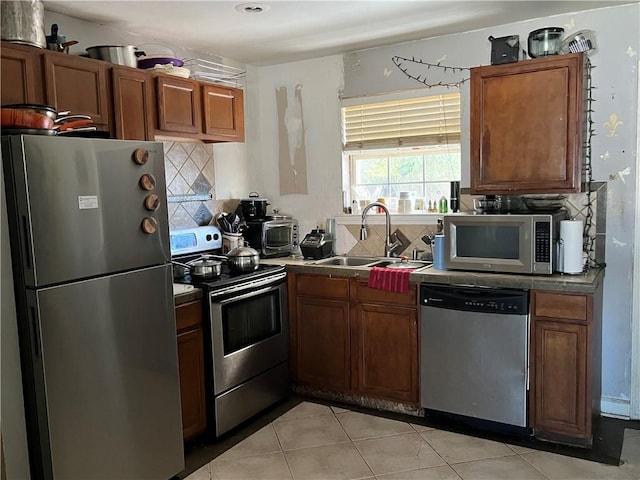 kitchen with appliances with stainless steel finishes, light tile patterned floors, decorative backsplash, and sink