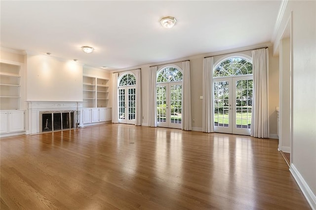 unfurnished living room with crown molding, built in features, french doors, and light hardwood / wood-style floors