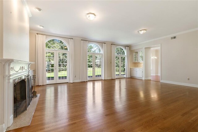 unfurnished living room featuring wood-type flooring, a premium fireplace, french doors, and crown molding