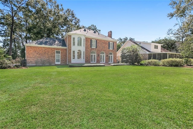 back of house featuring fence, a chimney, brick siding, and a yard