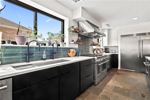 kitchen featuring wall chimney exhaust hood, sink, high end appliances, backsplash, and white cabinetry