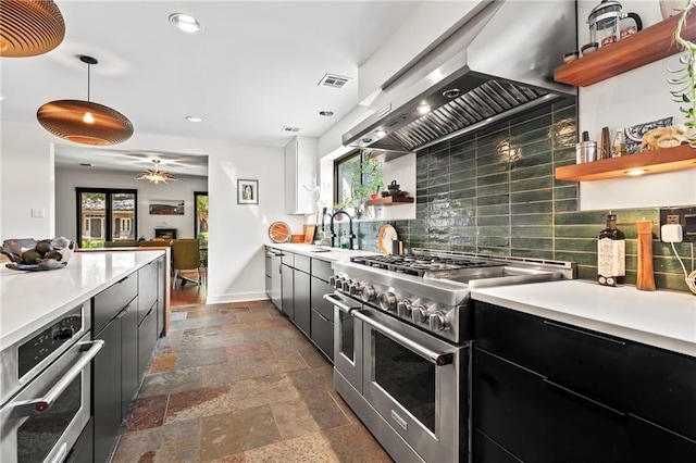 kitchen featuring stainless steel appliances, wall chimney exhaust hood, sink, pendant lighting, and backsplash