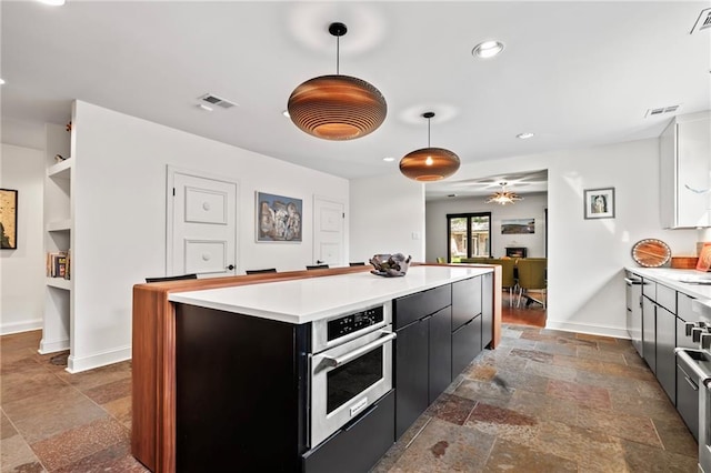 kitchen with stainless steel oven, hanging light fixtures, a center island, and ceiling fan