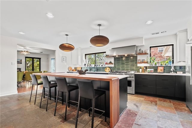 kitchen featuring plenty of natural light, wall chimney range hood, stainless steel range, and a center island