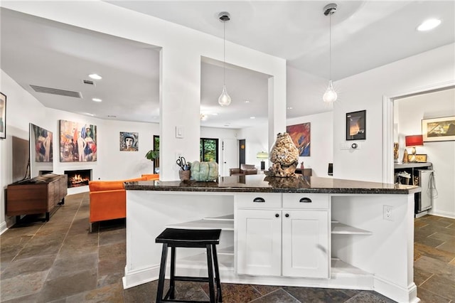 kitchen with kitchen peninsula, pendant lighting, dark stone counters, white cabinetry, and a kitchen breakfast bar