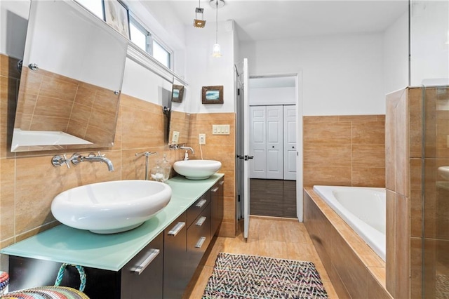 bathroom with hardwood / wood-style flooring, tile walls, vanity, and tiled bath