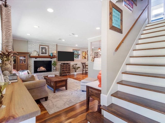 living room featuring a brick fireplace, hardwood / wood-style flooring, and crown molding