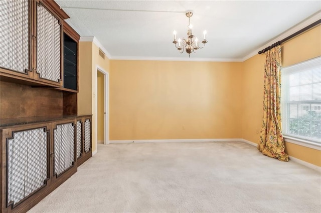 carpeted spare room with an inviting chandelier, ornamental molding, baseboards, and visible vents