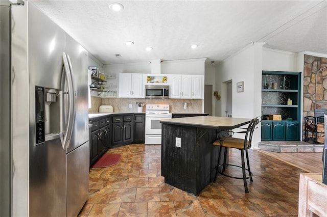 kitchen featuring a kitchen island, a breakfast bar, vaulted ceiling, stainless steel appliances, and white cabinetry